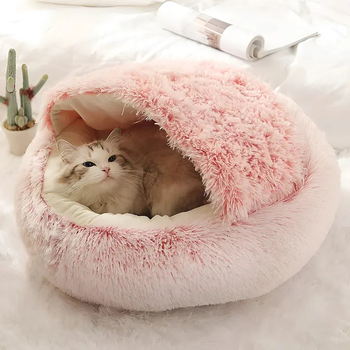 Un chat roulé en boule dans le panier igloo en peluche rose