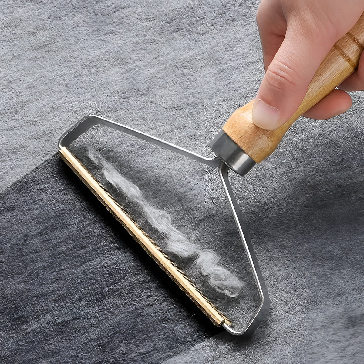 Main qui passe la brosse ramasse-poils en bois sur un tissu gris, les poils s’accumulent