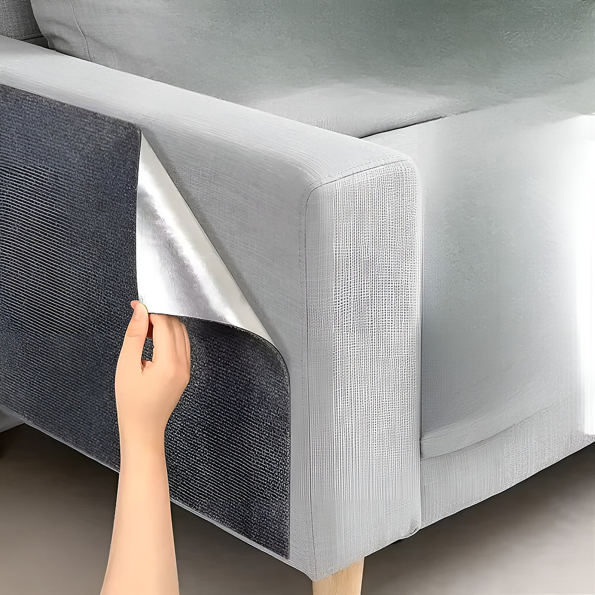 Main qui décolle le tapis griffoir adhésif gris collé sur le côté d’un canapé