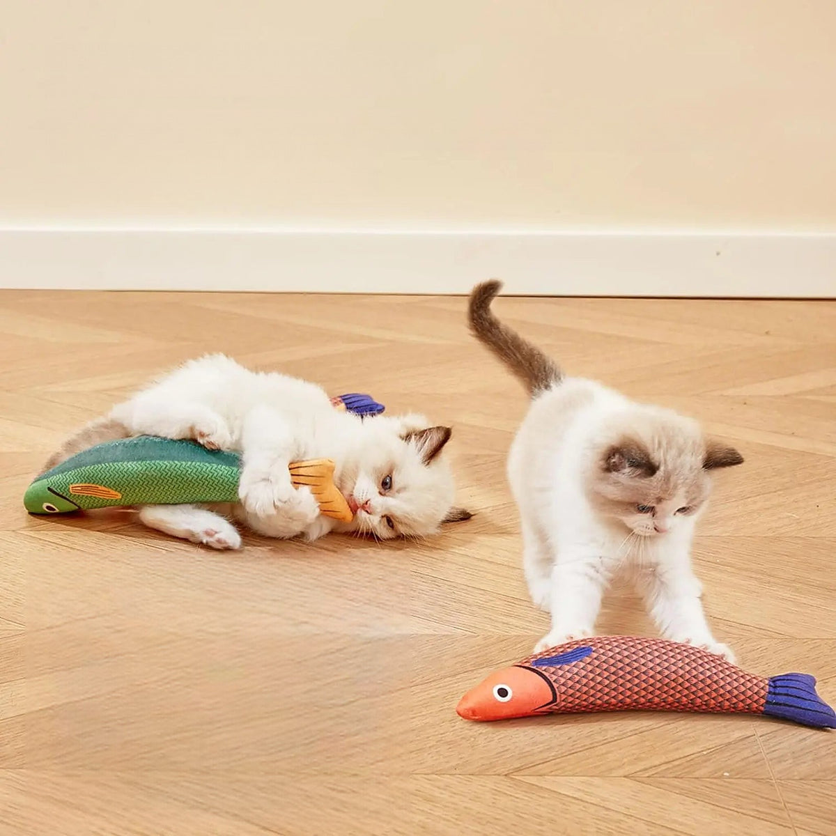 Deux chatons qui jouent avec des jouets poissons sur un parquet
